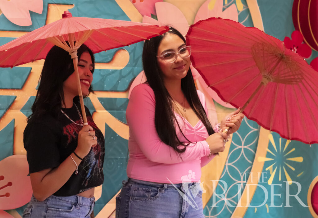 Reyna Martinez (left), a management freshman; and Viviana Almanza, an integrated health science freshman, take a photo with parasols at the photo booth during the Lunar New Year celebration Wednesday in the PlainsCapital Bank El Gran Sal贸n on the Brownsville campus. Mykel Del Angel/THE RIDER