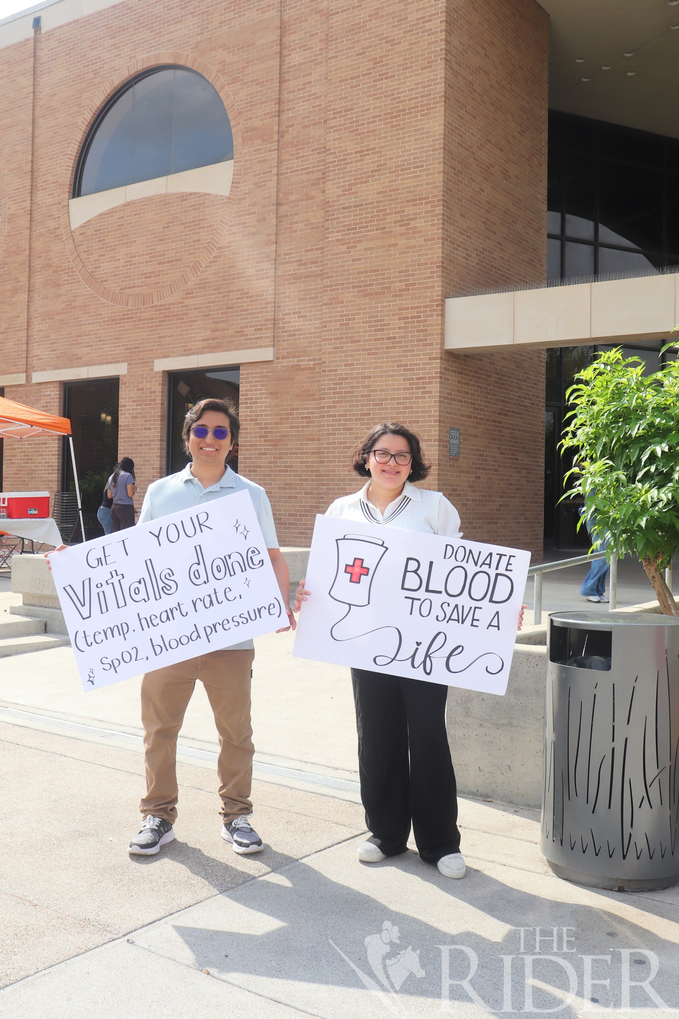 Christian Espinoza (left), a biology postbaccalaureate student, and Summer Segovia, a biology postbaccalaureate student, hold signs encouraging students and community members to donate blood Wednesday outside the Student Union on the Edinburg campus. 